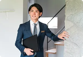 鞄を持ち、壁に手をかけながら遠くを見つめて笑みを浮かべるビジネスマン